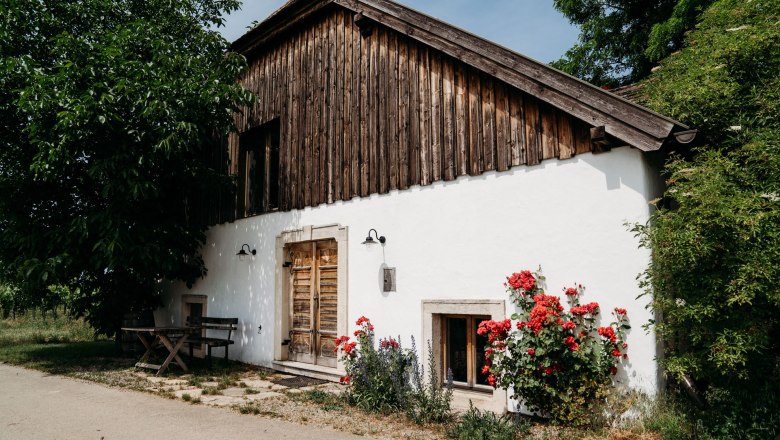 Exterior view, © Weinakademie Retz Exterior view of a house with wooden walls, white walls and red flowers in the foreground.