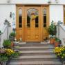 Front of a house with wooden door, staircase and floral decoration.