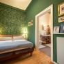 Cozy bedroom with green patterned wallpaper, double bed and adjoining bathroom.