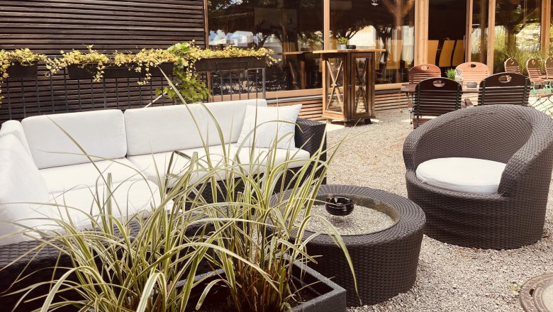 Cozy outdoor lounge with white sofas, round tables and plants.