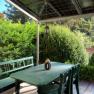 Terrace with green table and benches, surrounded by bushes and trees, with solar panel roof.