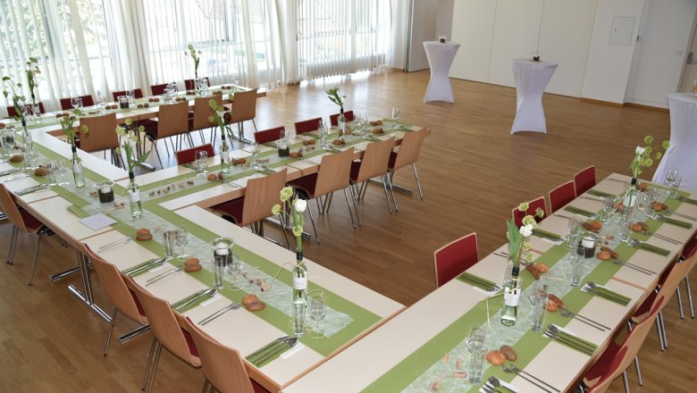 A festively decorated hall with tables arranged in a U-shape, green table runners and floral decorations.
