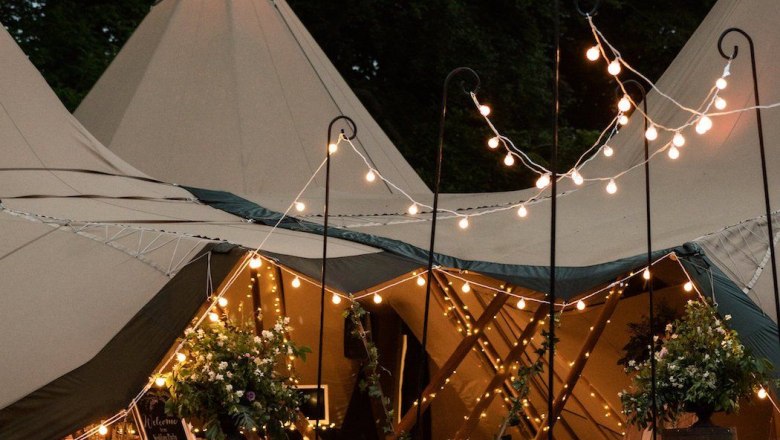An illuminated teepee tent for an event, surrounded by plants and fairy lights.