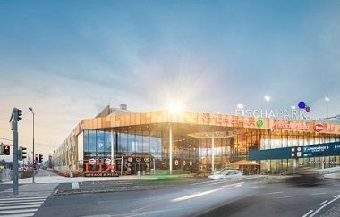Front view of the Fischapark shopping center with modern glass façade and illuminated signs.