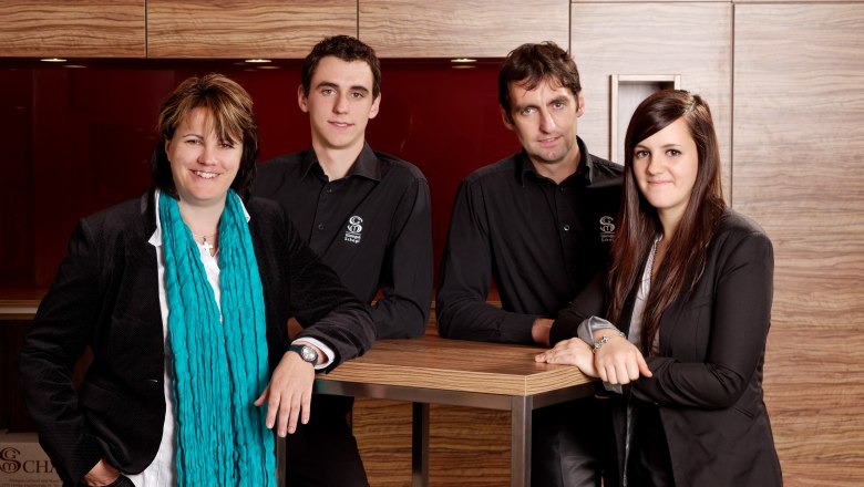 Four people stand smiling in front of a wooden wall.