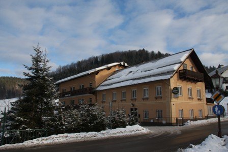 A yellow building in the snow with the inscription 'Pension zur Post'.