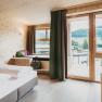 Modern hotel room with wooden walls, large bed and balcony with mountain view.