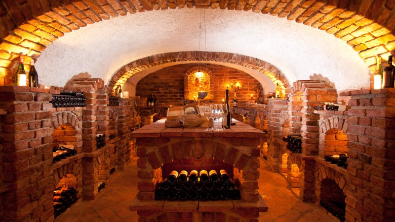 An atmospherically lit wine cellar with brick walls and wine bottles on shelves.