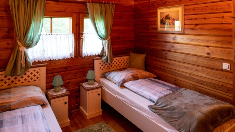 Cozy bedroom with wooden walls, two single beds, green curtains and bedside tables with lamps.