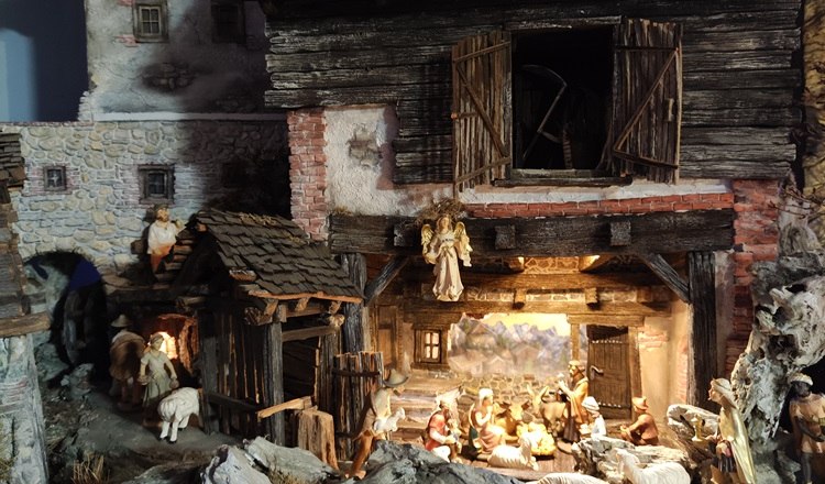 Detailed nativity scene with figures in a rustic barn, surrounded by sheep and shepherds.