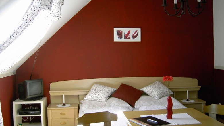 Cozy bedroom with red wall, bed, table and TV.