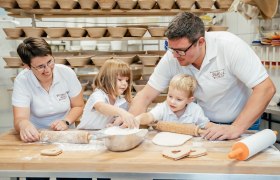 Family baking in a bakery with many bread baskets in the background.