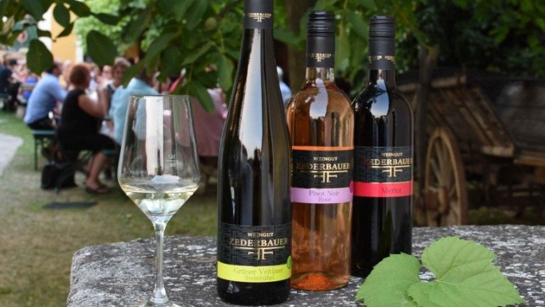 Three bottles of wine and a glass on an outdoor table, with people in the background.