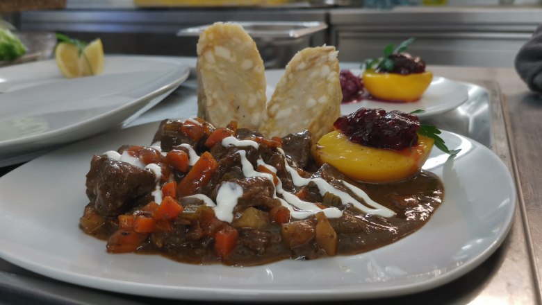 A plate with a meat dish, garnished with sauce, vegetables and a peach half with cranberries.