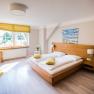 Bright double room with wooden bed, yellow pillows and large window.