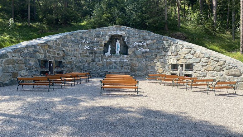 Stone grotto with a statue of the Virgin Mary and benches outside.