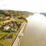 Aerial view of a riverbank with houses and mobile homes, surrounded by green countryside.
