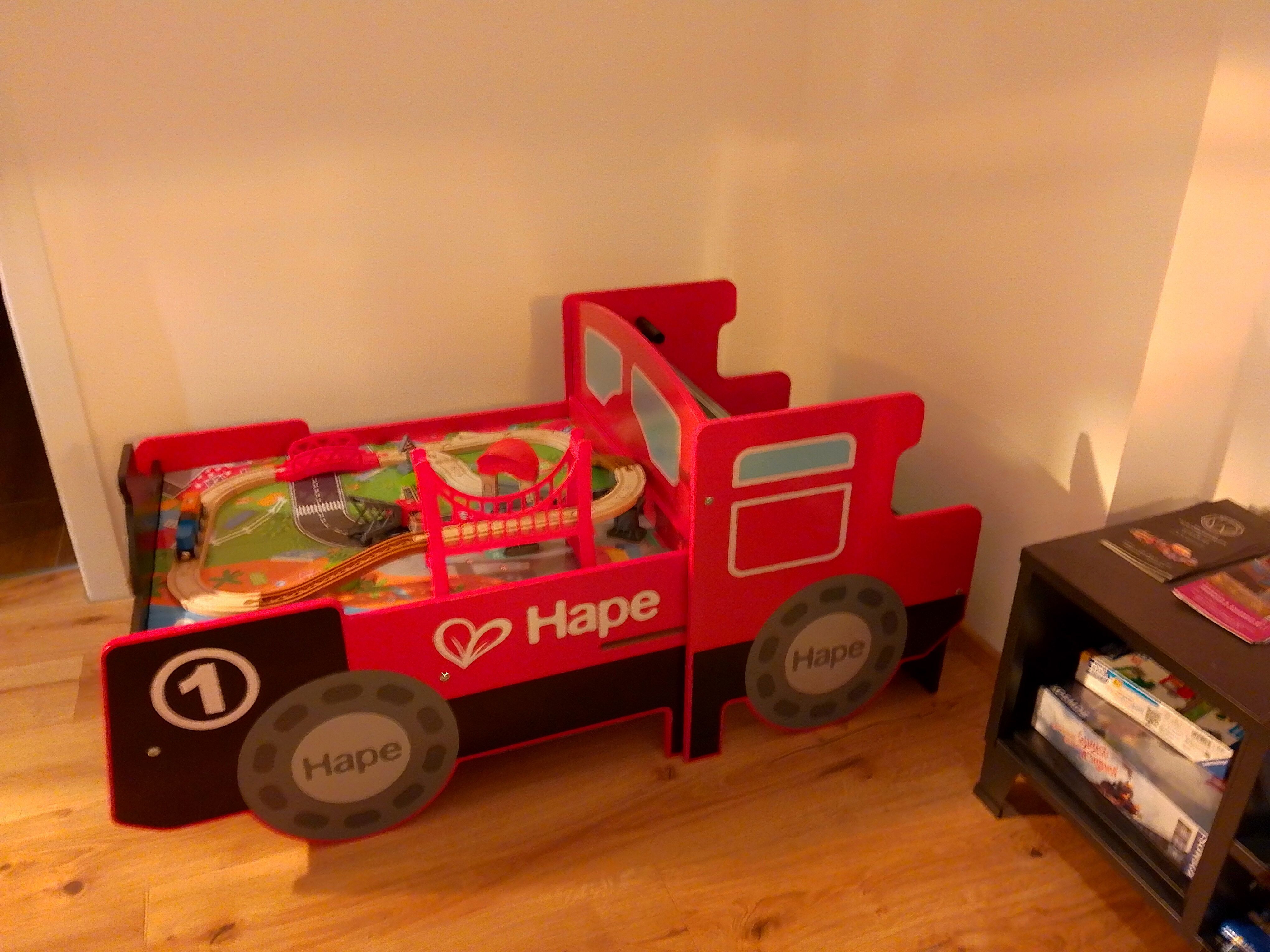 Red toy bed in the shape of a locomotive with toy train.