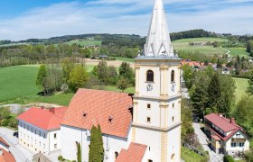 Aerial view of the fortified church of Krumbach in a rural setting with green fields and blue sky.