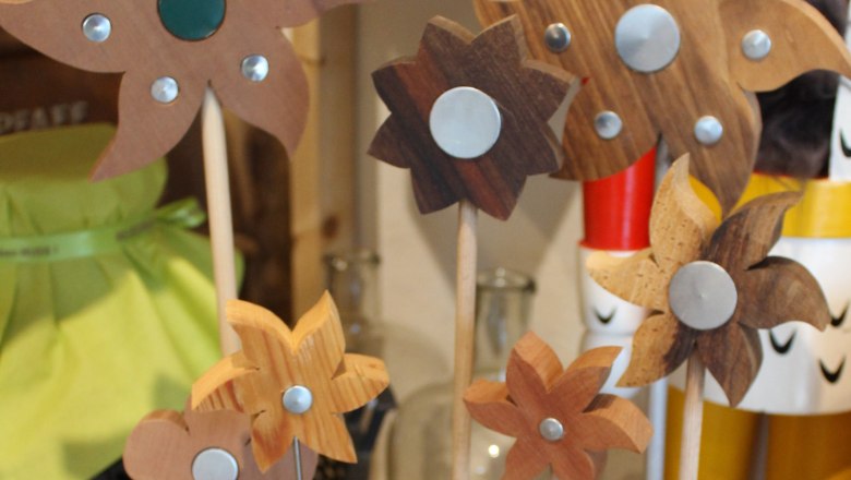 Wooden flowers with metal decorations on rods on a shelf.