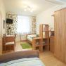 A bright bedroom with wooden furniture, two beds, a desk and a small TV on the wall.