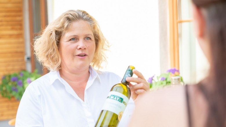 A woman holds a bottle of wine and talks to another person.