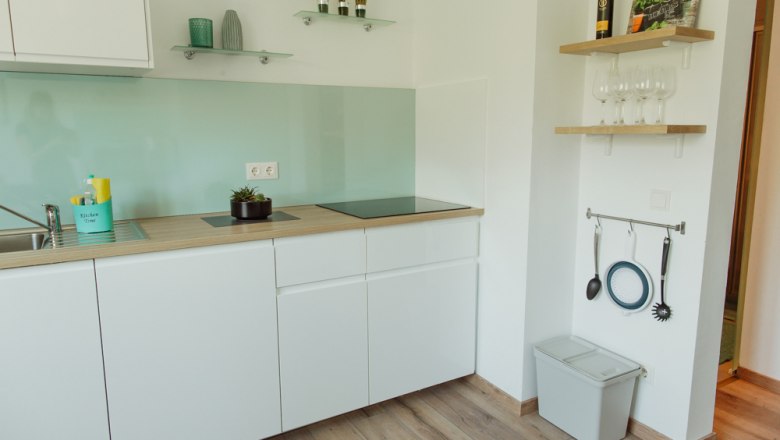Modern kitchen with white cupboards, glass splashback and wooden shelves.