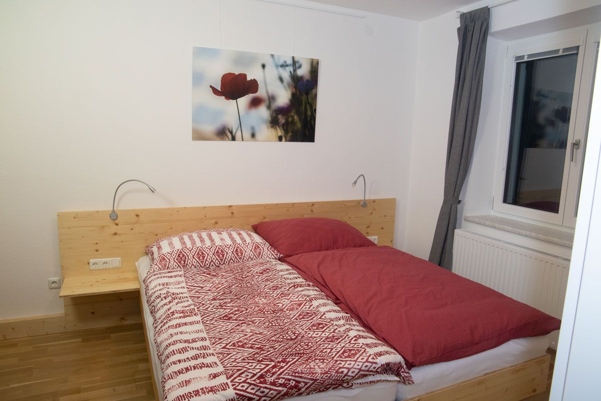 Bedroom with double bed, red bed linen and a picture of poppies on the wall.