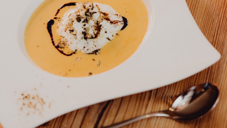 Pumpkin soup with cream and pumpkin seed oil in a white plate on a wooden table.