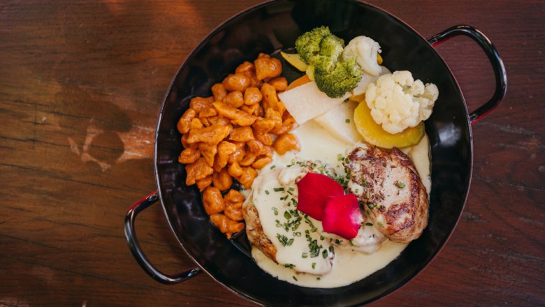 Pork medallions with cheese sauce, red spaetzle and garden vegetables in a black pan.