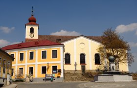 Church with yellow fa&ccedil;ade and tower with red roof on a main square.