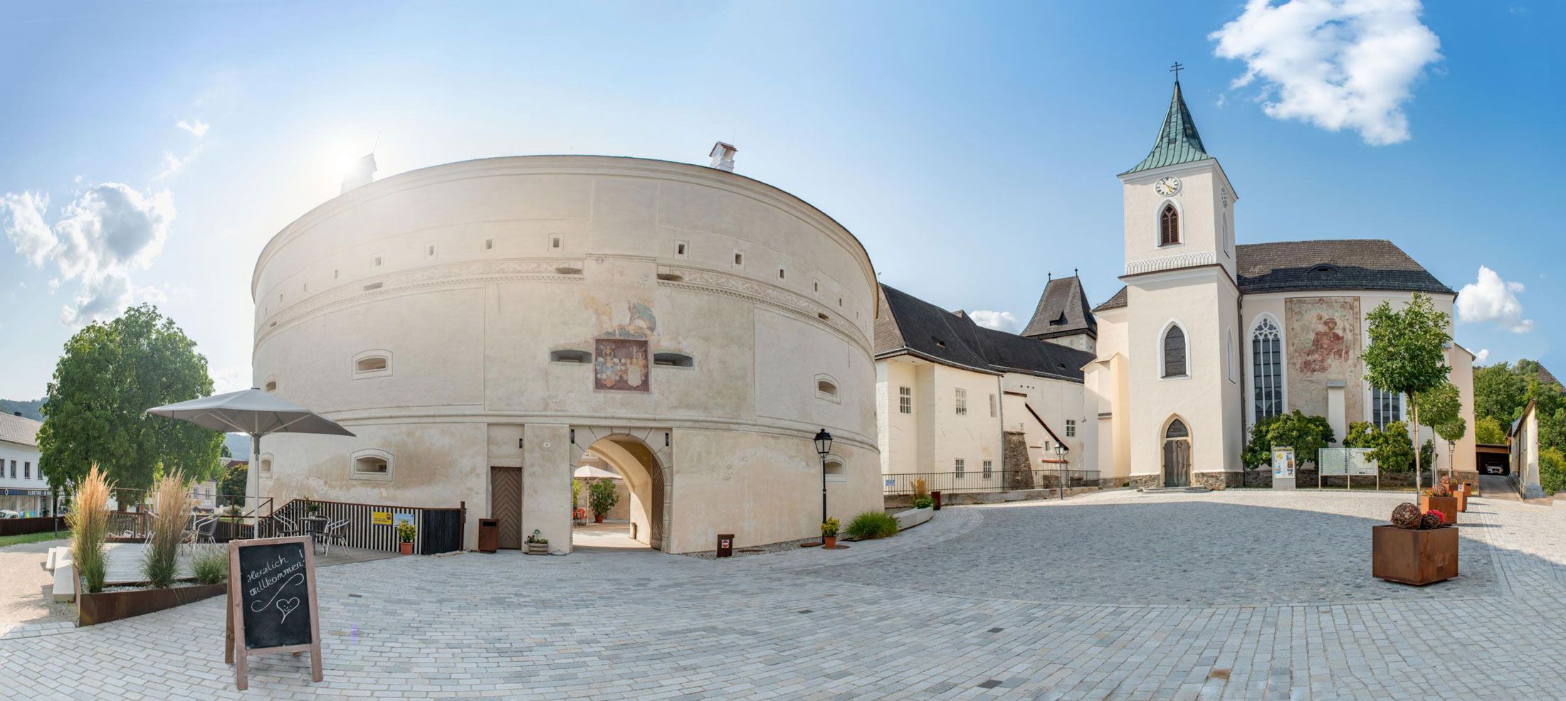 Panoramic view of Pöggstall Castle with round tower and church in sunny weather.