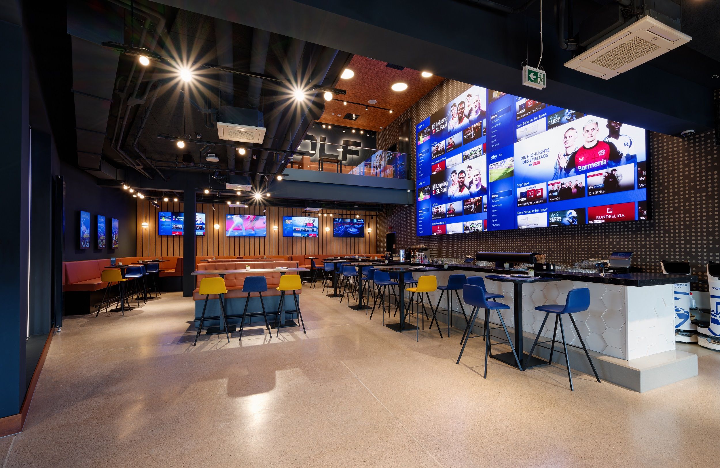 Interior view of a modern sports bar with large screens and colorful chairs.