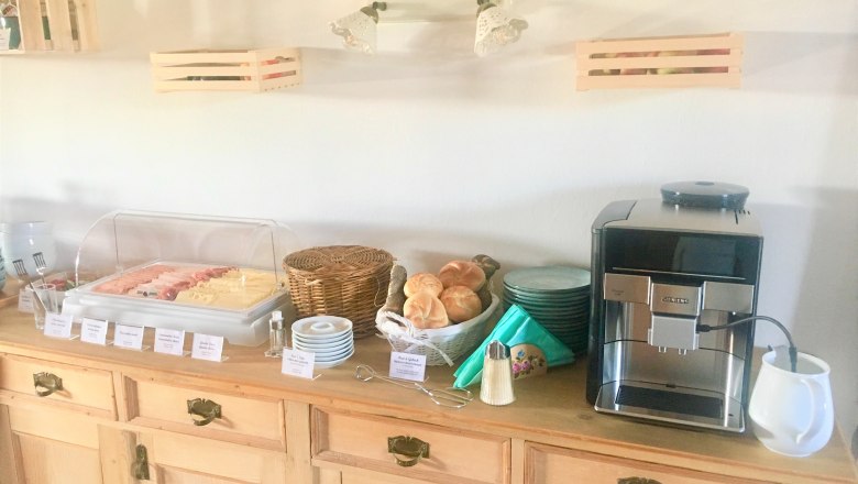 Breakfast buffet with cold cuts, bread rolls and coffee machine on a wooden table.