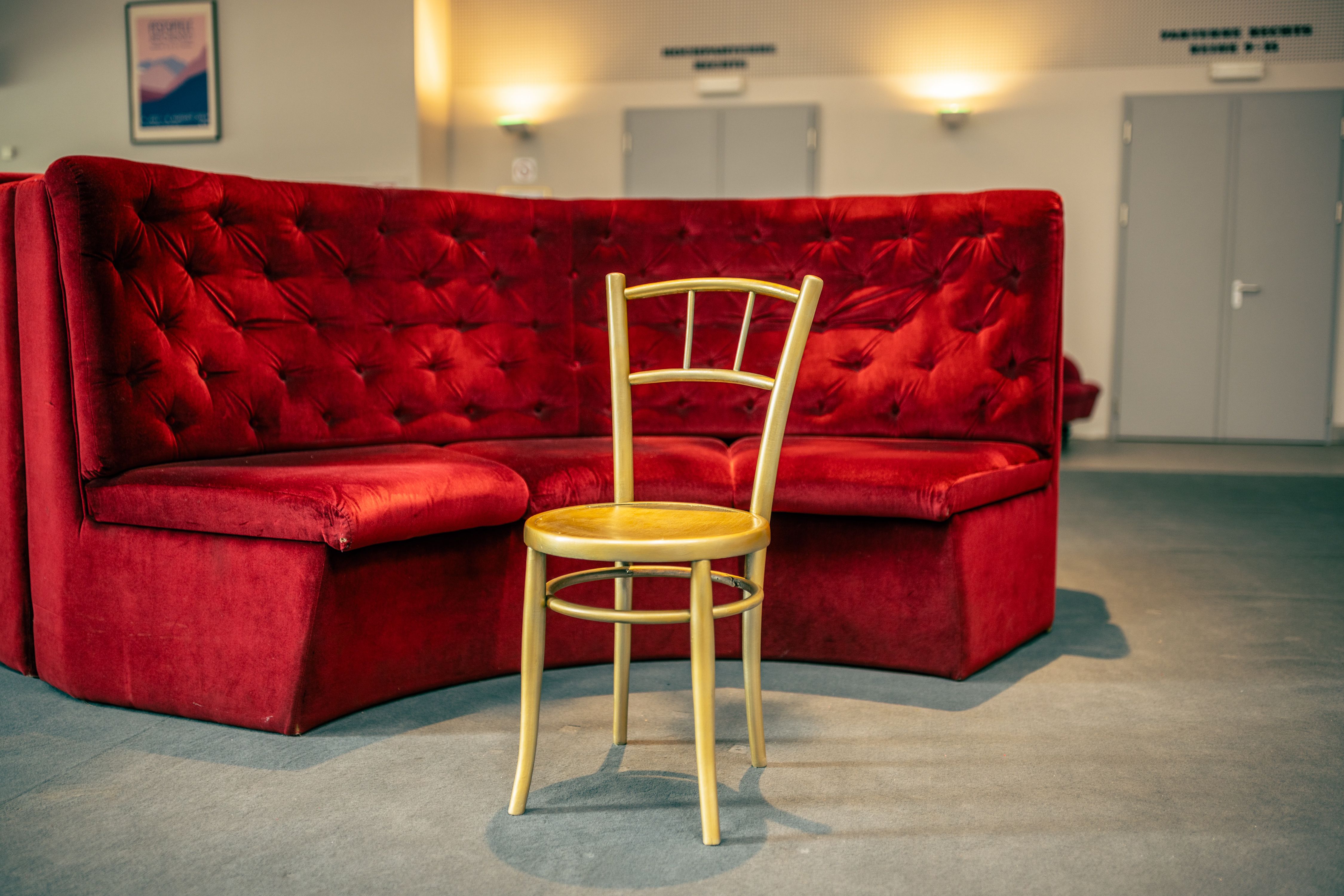 A single wooden chair stands in front of a red velvet bench in a theater foyer.