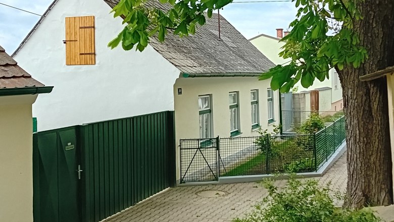 A traditional white cottage with a green fence and tree in the foreground.