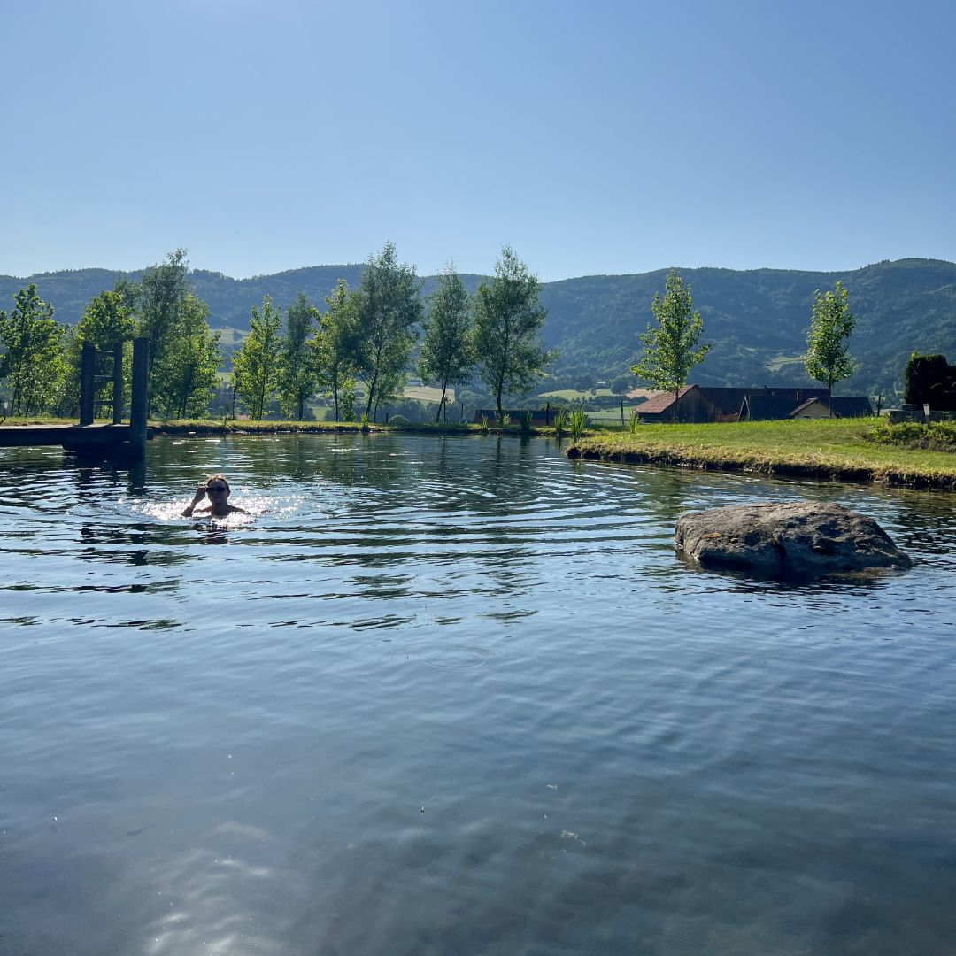 Person swimming in a pond with trees and hills in the background.