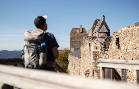 A hiker with a rucksack looks at the ruins of Aggstein Castle on a sunny day.