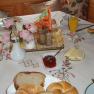 A laid breakfast table with bread rolls, cold cuts, cheese, jam, orange juice and flowers.