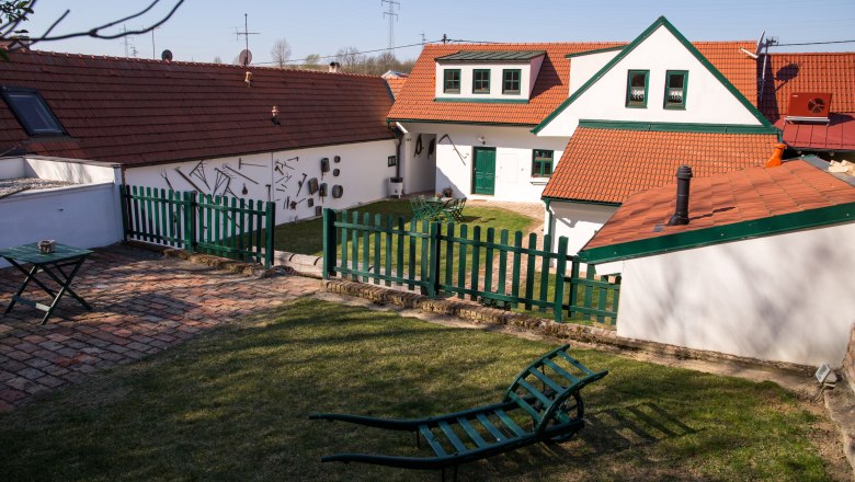 A traditional vineyard with red tiled roofs, green fences and garden furniture on a meadow.