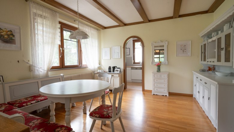 Dining area in a vacation home with wooden floor, white furniture and red upholstery.