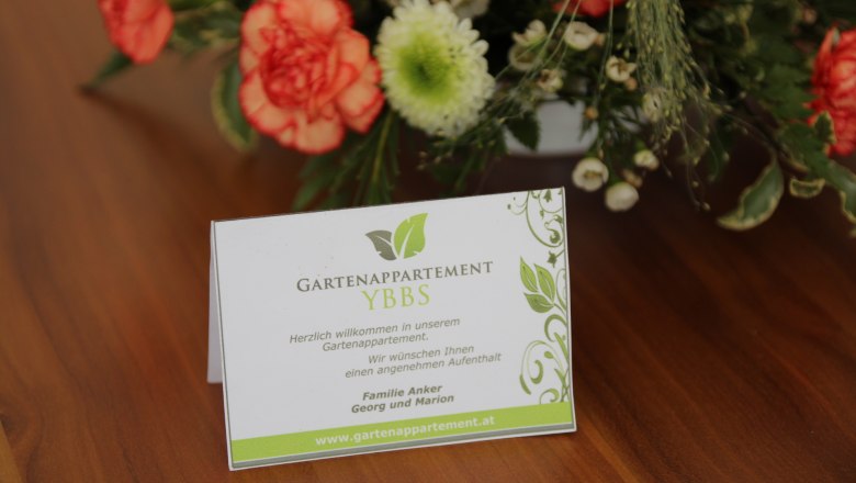 Welcome card of the Gartenappartement Ybbs on a table with flowers.