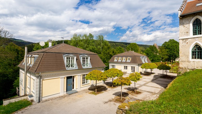 Cavalier houses, © Wiener Alpen / Christian Kremsl Two manor houses with mansard roofs and well-tended trees in the foreground, surrounded by green countryside and blue sky.