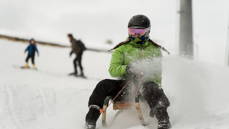 Person wearing a green anorak and helmet riding a sledge in the snow.