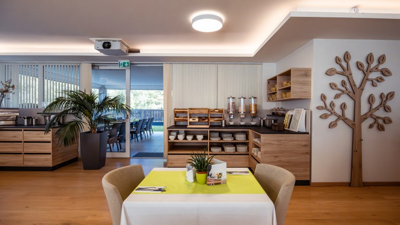 Interior view of a hotel restaurant with breakfast buffet and decorative wooden element on the wall.