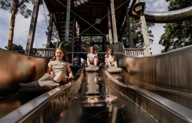 Three children slide down a metal slide in a park.