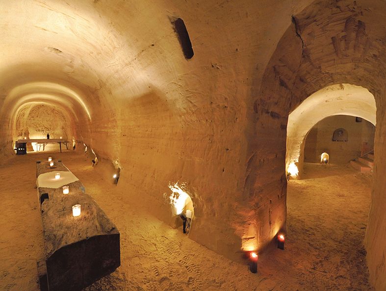 Underground sandstone cellar with candlelight and rustic tables.