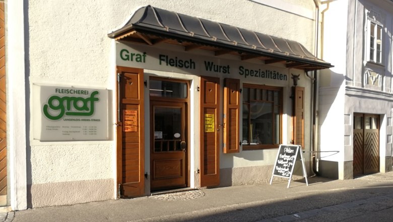 Exterior view of the Graf butcher's shop with wooden doors and advertising board.
