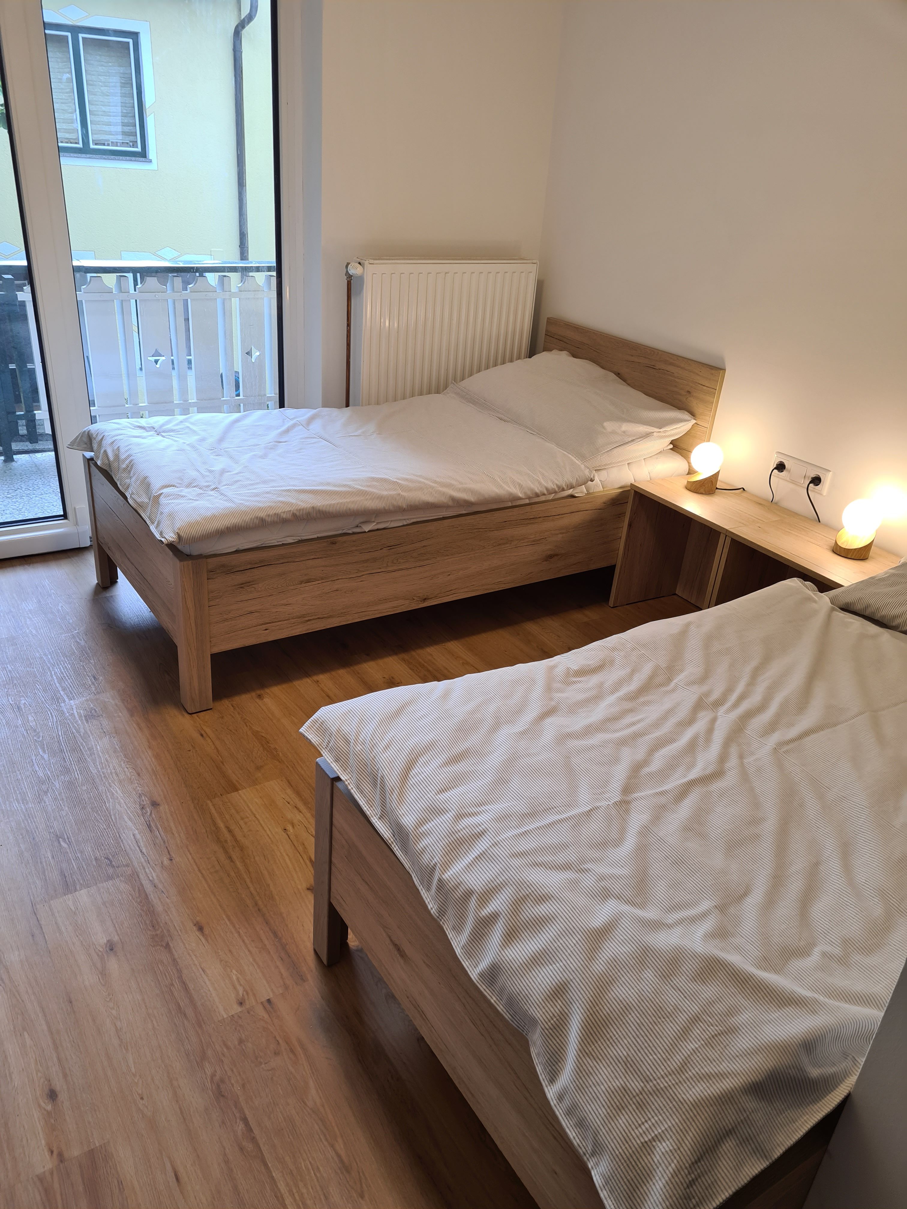 Two single beds in a bright room with wooden floor and balcony access.