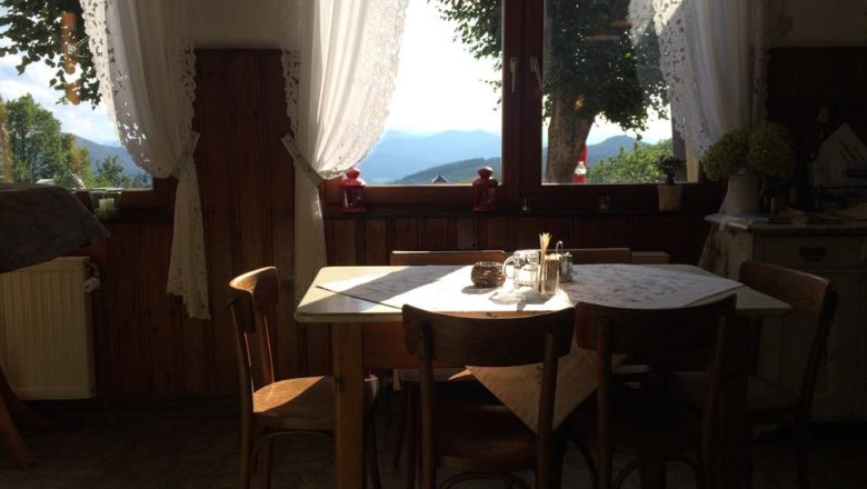 A cozy dining area with a wooden table and chairs in front of a large window with a view of the mountains and trees.